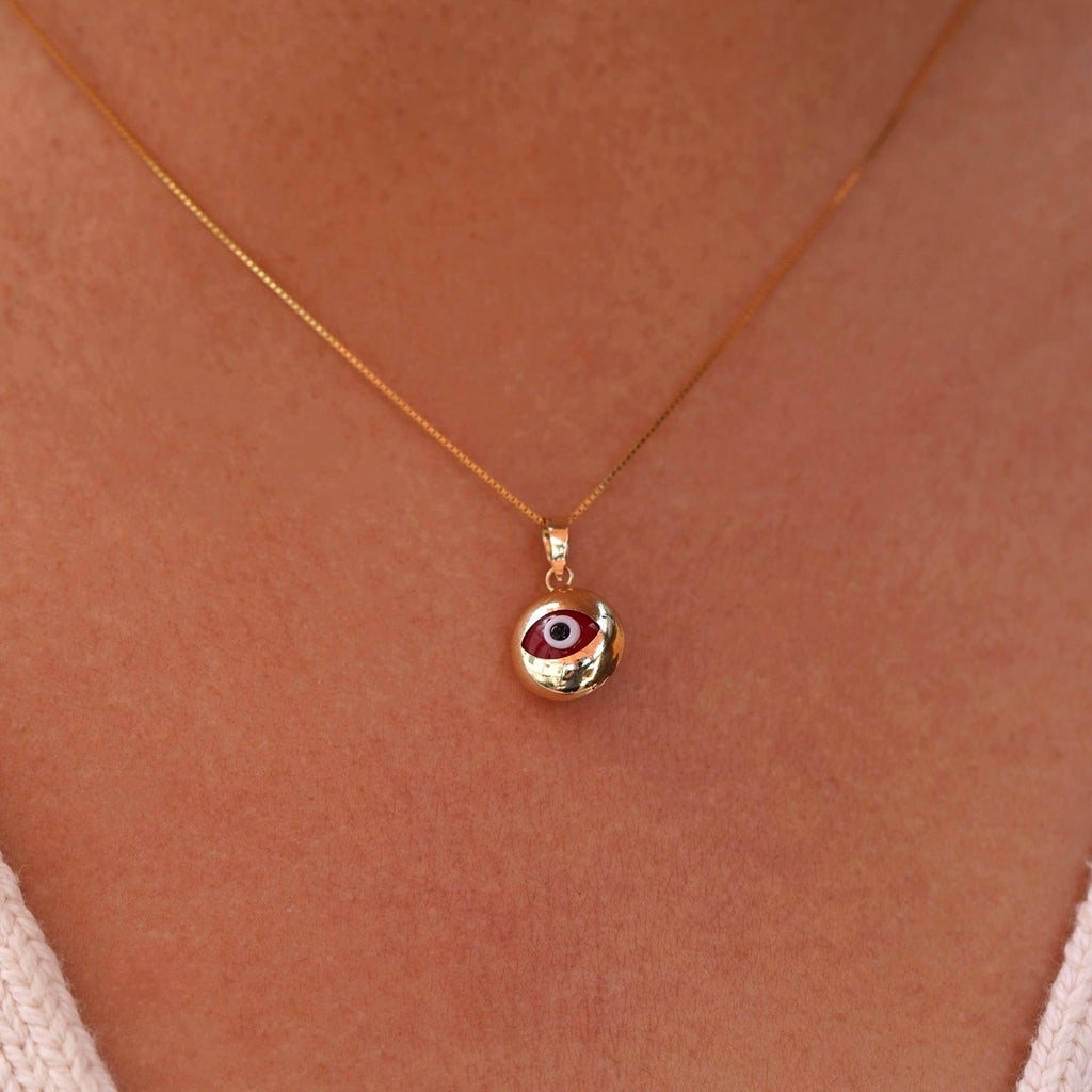 A model wearing a 14K yellow gold evil eye pendant with a red zirconia center on a fine gold chain, resting elegantly at her collarbone. The polished gold finish reflects light beautifully, highlighting the pendant’s delicate craftsmanship, symbolic protection, and subtle luxury from Tehrani Jewelry.