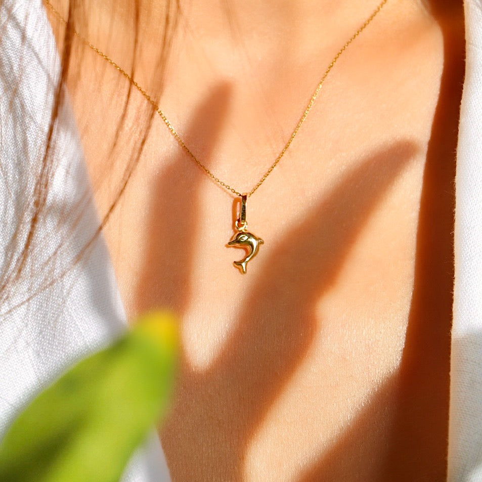 Model wearing the 14K yellow gold dolphin pendant on a fine chain, demonstrating its dainty size and stylish appeal.