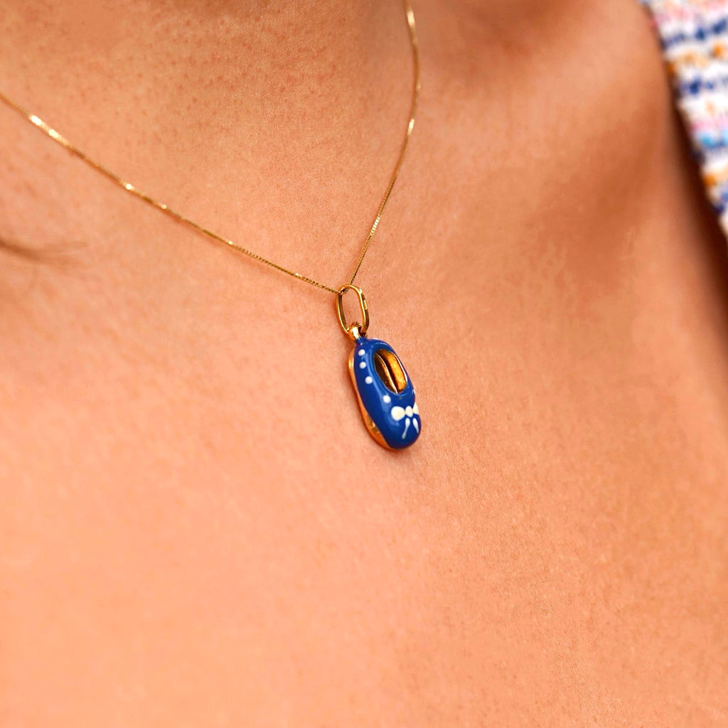 A model wearing a delicate 14K gold baby shoe pendant with blue enamel on a thin gold chain. The pendant is the focal point, elegantly styled and perfect for daily wear or special occasions, with the model showcasing its charm and grace.