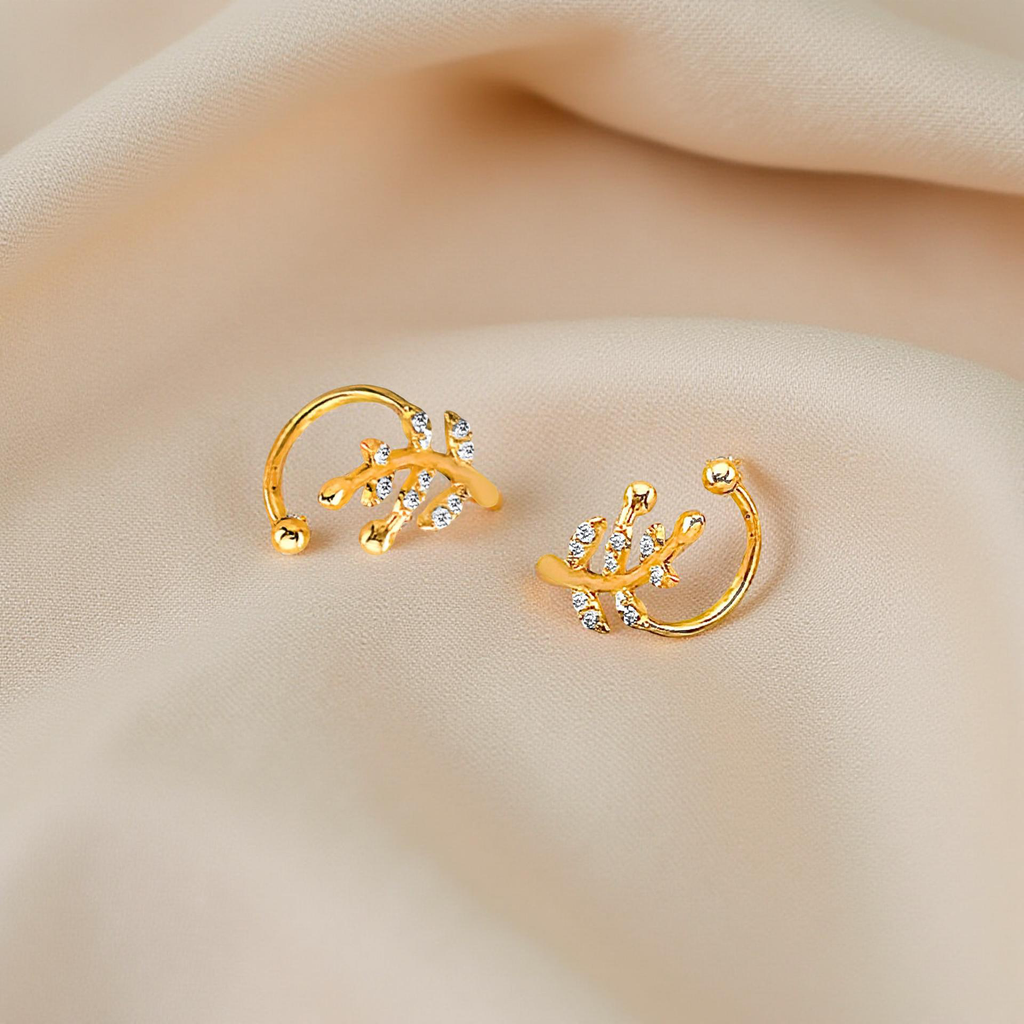 4K gold CZ leaf ear cuff resting on beige cloth, highlighting its sparkling leaf design and soft polished gold.