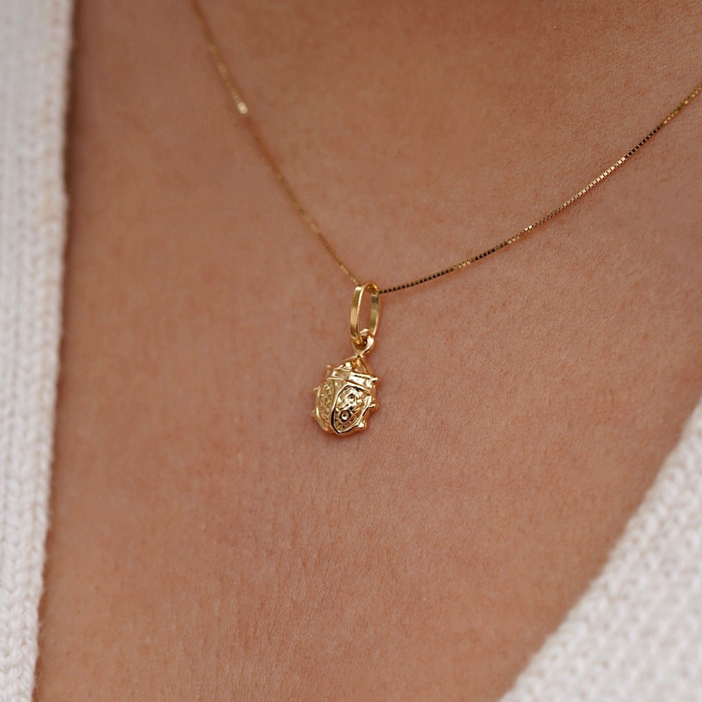 Model wearing a delicate 14K gold ladybird pendant on a fine chain, showcasing its dainty size and polished gold shine against the neckline.