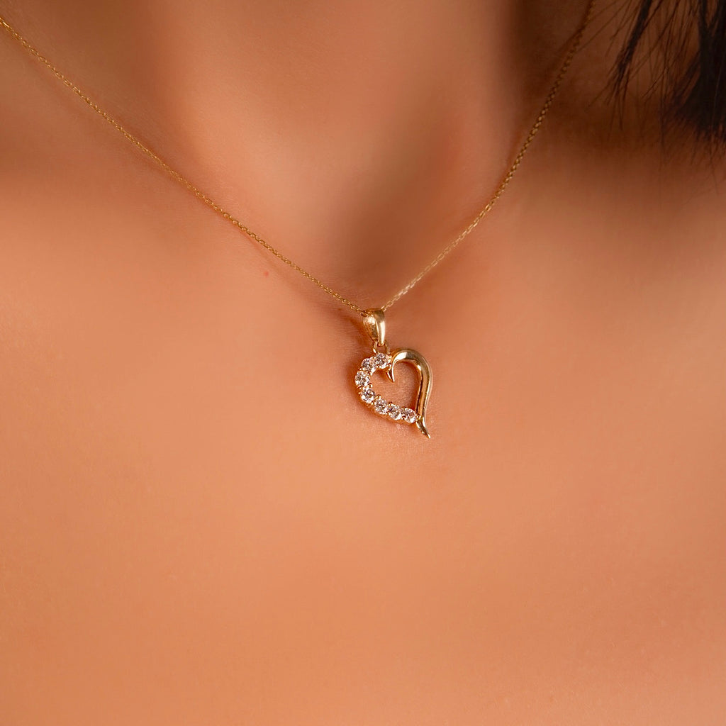 A delicate 14K Solid Yellow Gold Tiny Heart Pendant worn by a model, elegantly resting on a fine gold chain. The charm’s minimalist heart shape and sparkling cubic zirconia catch the light, adding a touch of love and sophistication to any outfit.