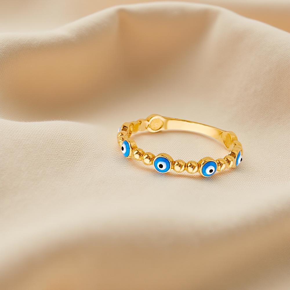 A delicate 14K yellow gold evil eye ring with a light blue enamel center is elegantly displayed on an off-white cloth, highlighting its smooth, polished finish and minimalist protective design—symbolizing spiritual shielding and modern style.