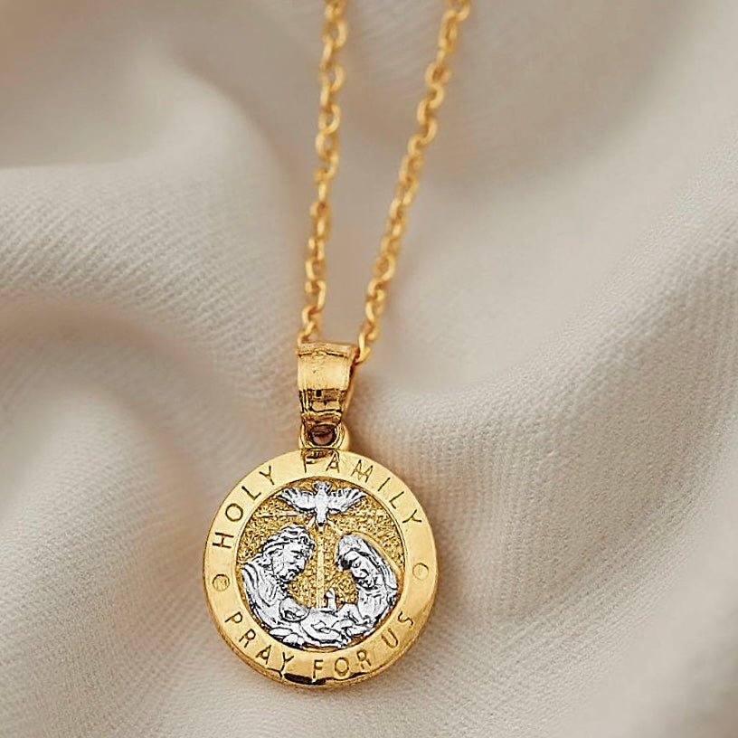Close-up of the 14K gold Holy Family round medallion on textured off-white cloth, focusing on the delicate two-tone details of the Virgin Mary, Joseph, and baby Jesus.