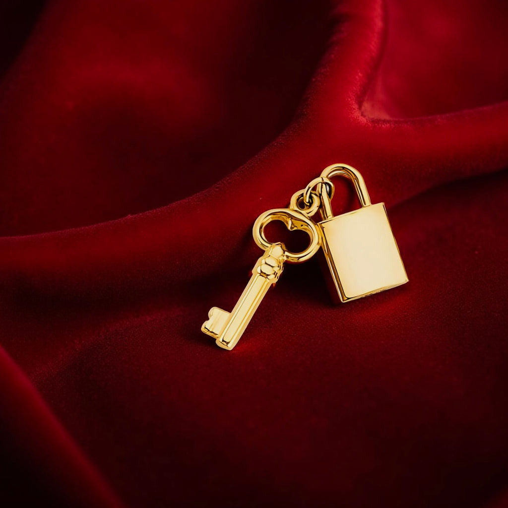 14K yellow gold lock and key pendant resting on a dark red velvet cloth, showcasing the delicate polished finish and symbolic charm in warm lighting.
