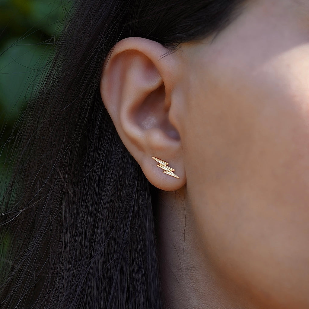 Model wearing 14K gold thunderbolt earrings, showcasing their trendy lightning bolt shape and dainty fit on the ear.