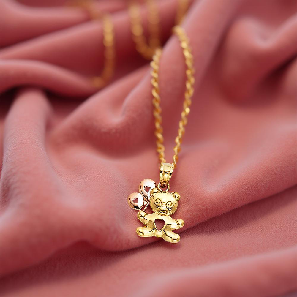 14K gold baby bear pendant with balloon resting on pink velvet fabric, showcasing its polished finish and whimsical design.