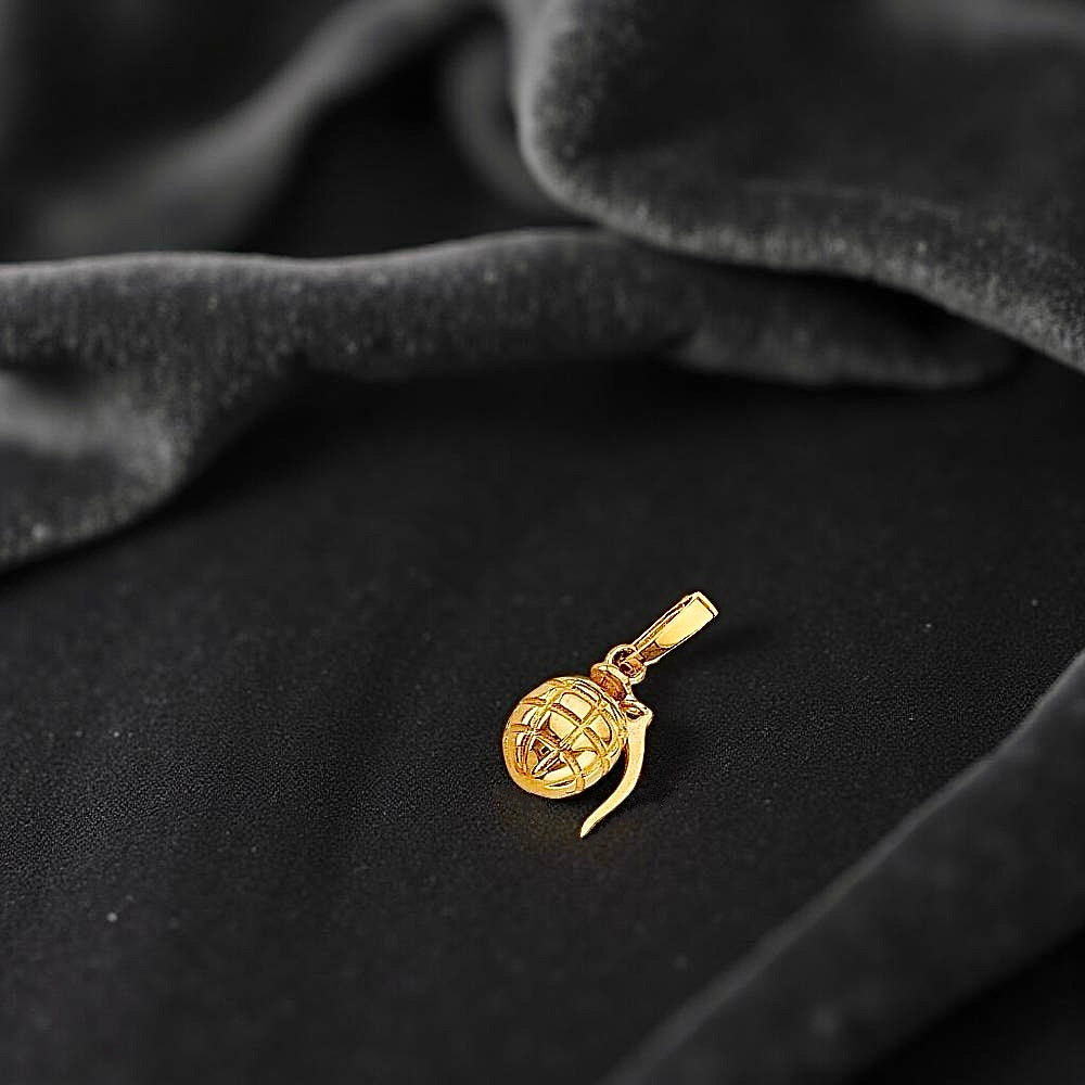 Miniature gold grenade charm placed on a black fabric, showing off its realistic shape and reflective surface.