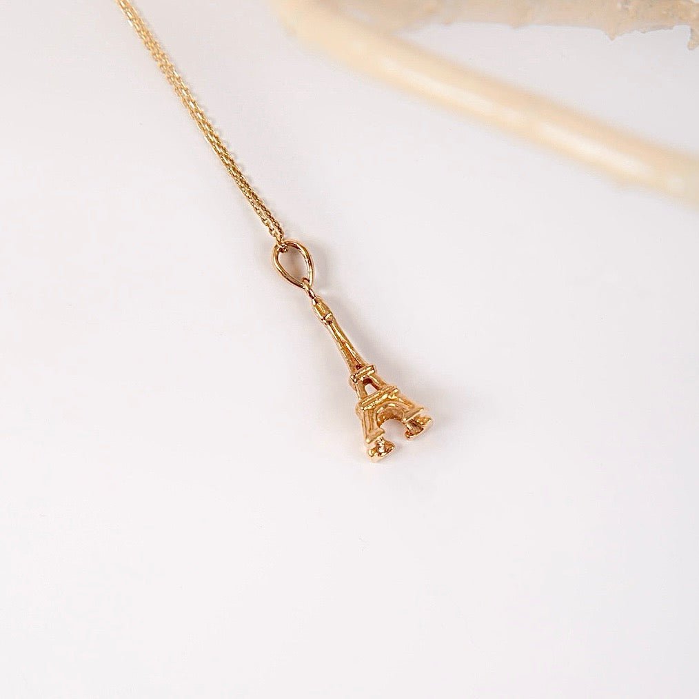 A 14K yellow gold Eiffel Tower pendant displayed against a plain background, highlighting its intricate detailing and polished finish.