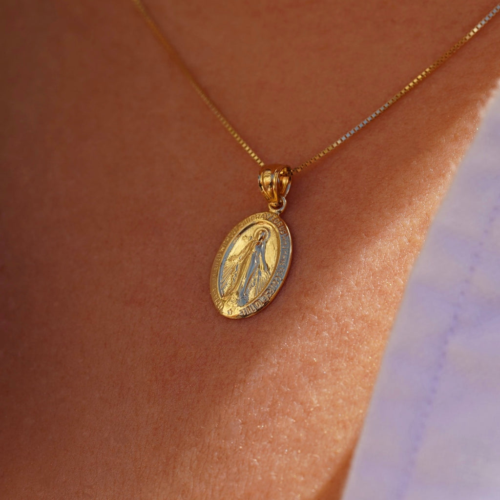 Model wearing a 14K gold Milagrosa pendant on a fine gold chain, the lightweight medallion resting at the collarbone, adding a subtle yet meaningful touch of faith.