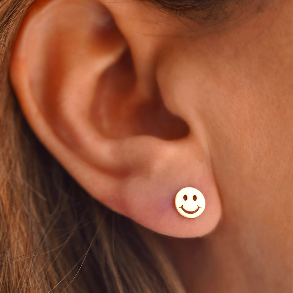 Close-up of a model wearing the 14K Yellow Gold Smiling Emoji Stud Earrings, showcasing their fun and playful design with a secure screw-back closure.