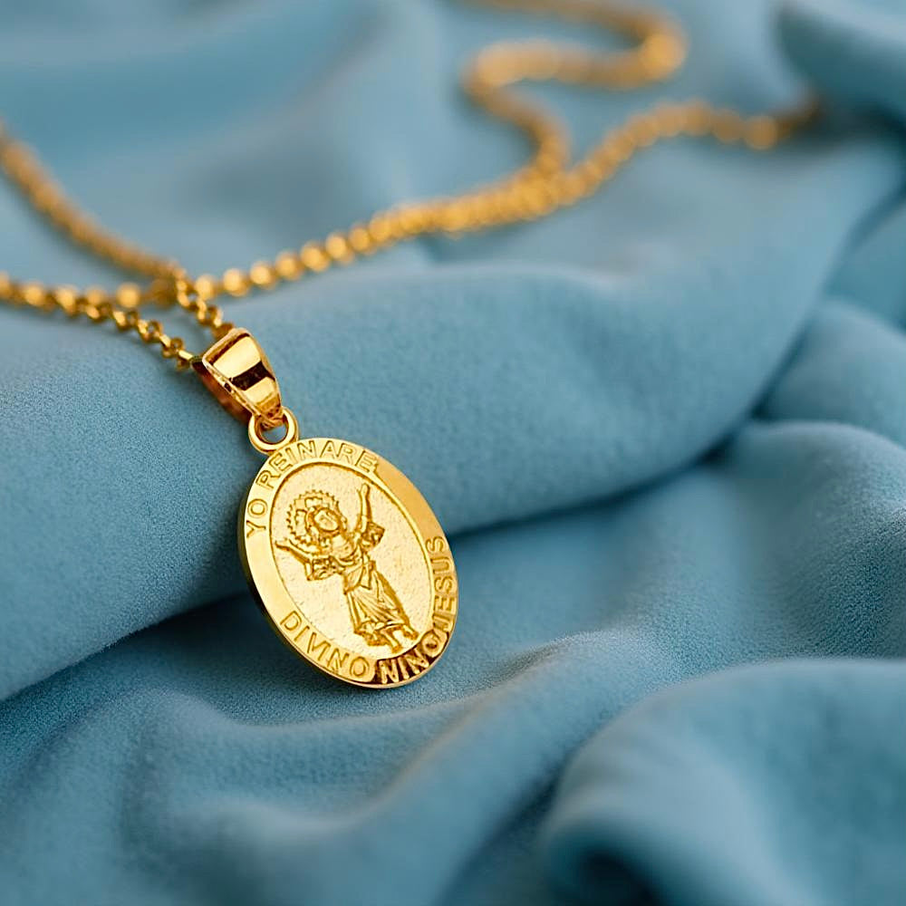 14K yellow gold Baby Jesus pendant displayed on a soft blue velvet surface, showcasing its smooth finish and elegant religious detail.