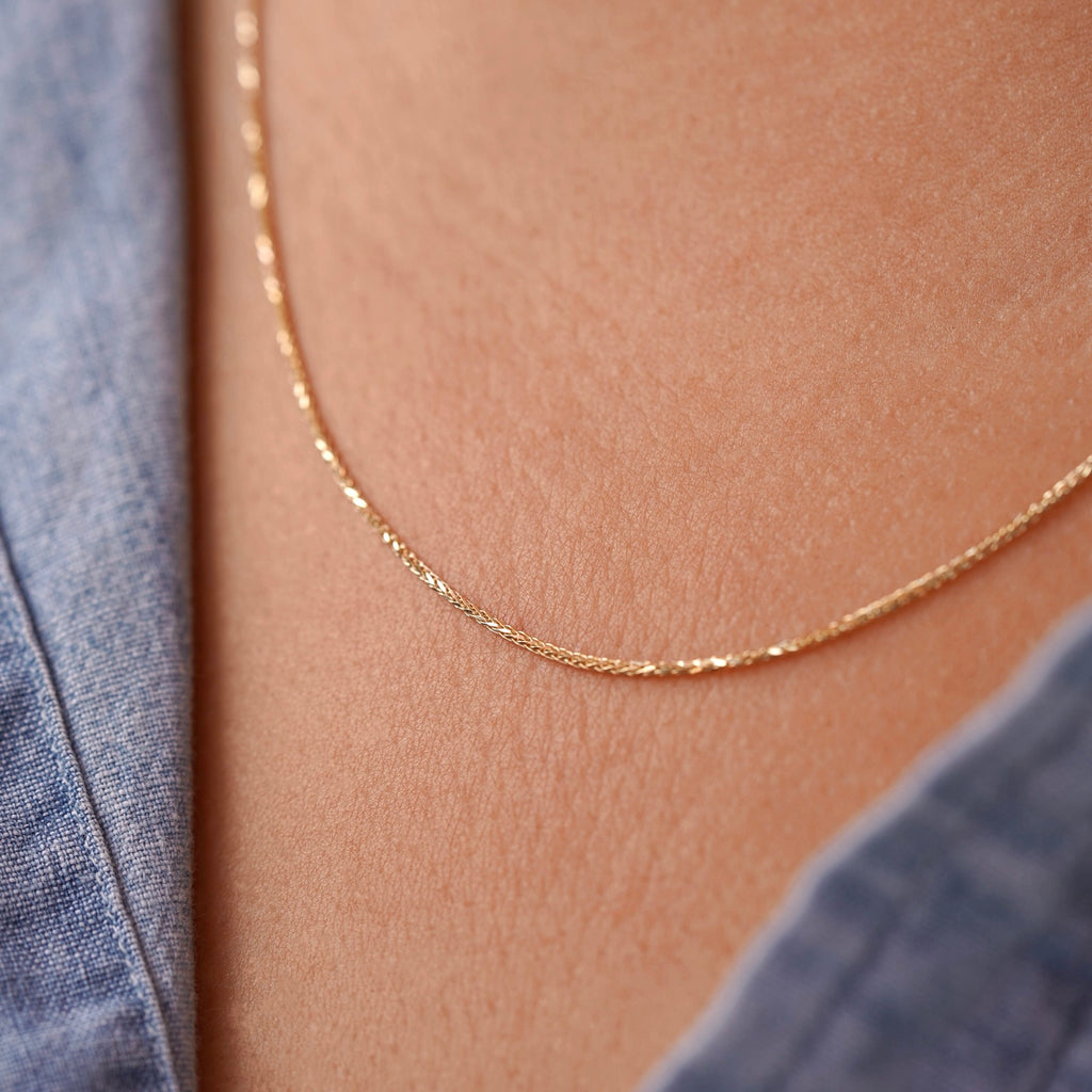 A model wearing a 14K yellow solid gold wheat chain necklace with 1.5mm flat open links, styled with a casual outfit to show the necklace’s versatility for both everyday and formal wear.