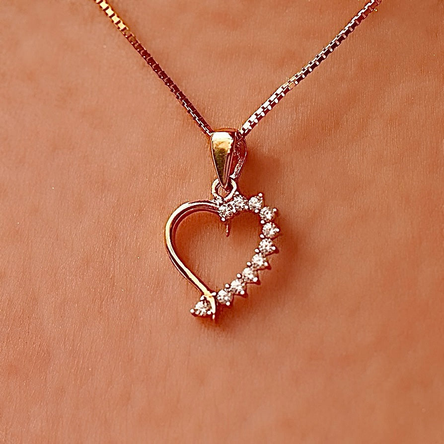 A delicate 14K Gold CZ Heart Pendant worn on a fine chain, elegantly resting against a model’s neckline, highlighting its dainty and elegant design.