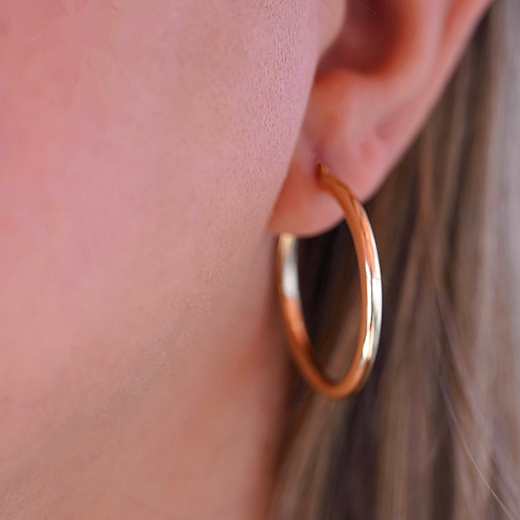 A stylish woman wearing 14K gold hoop earrings in yellow and white gold, adding a touch of sophistication to her everyday look.