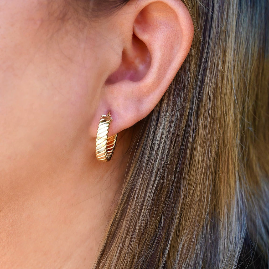 A woman elegantly wearing a pair of 14K solid gold Huggies hoop earrings. The 20mm hoops hug her earlobes perfectly, complementing her effortless style with a touch of timeless luxury.