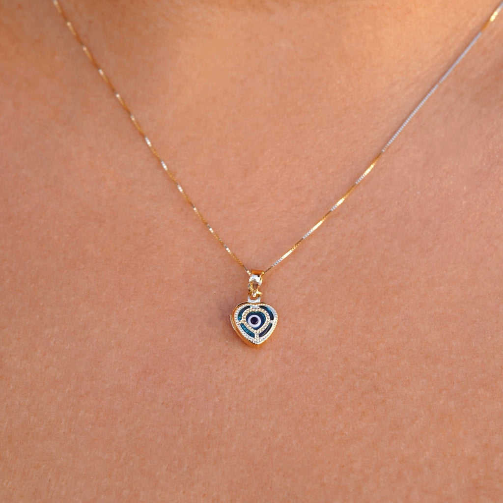 Model wearing a 14K yellow gold heart pendant with an evil eye center, showcasing elegant shine and dainty design against the skin.