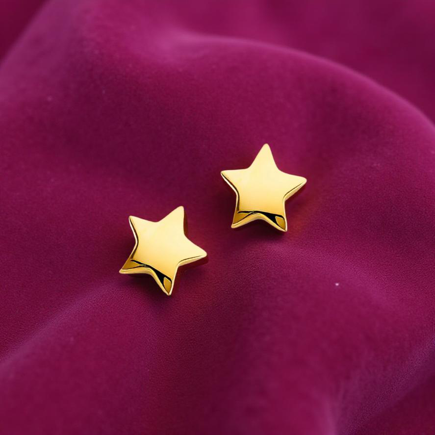 14K gold star earrings laying flat on a magenta velvet cloth, highlighting their polished shine and delicate size.