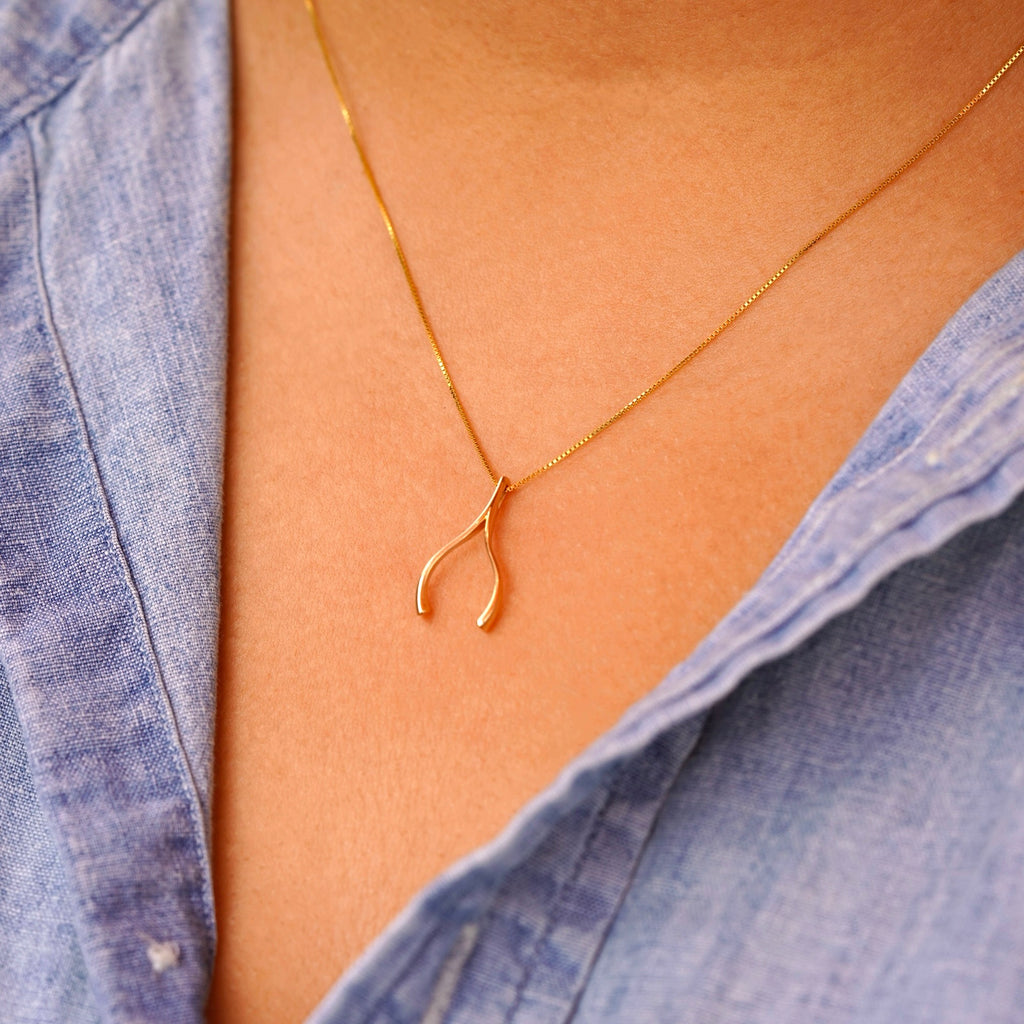 Model wearing the 14K gold wishbone pendant on a delicate chain, demonstrating its dainty size and elegant everyday look.