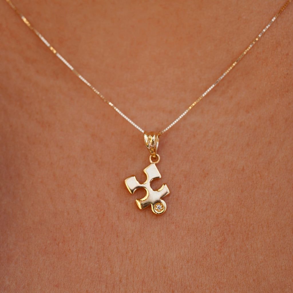A model gracefully wears the 14K gold puzzle piece pendant on a fine chain, showcasing its subtle elegance and timeless design. The charm rests beautifully against the skin, adding a touch of meaning and sophistication to any outfit.