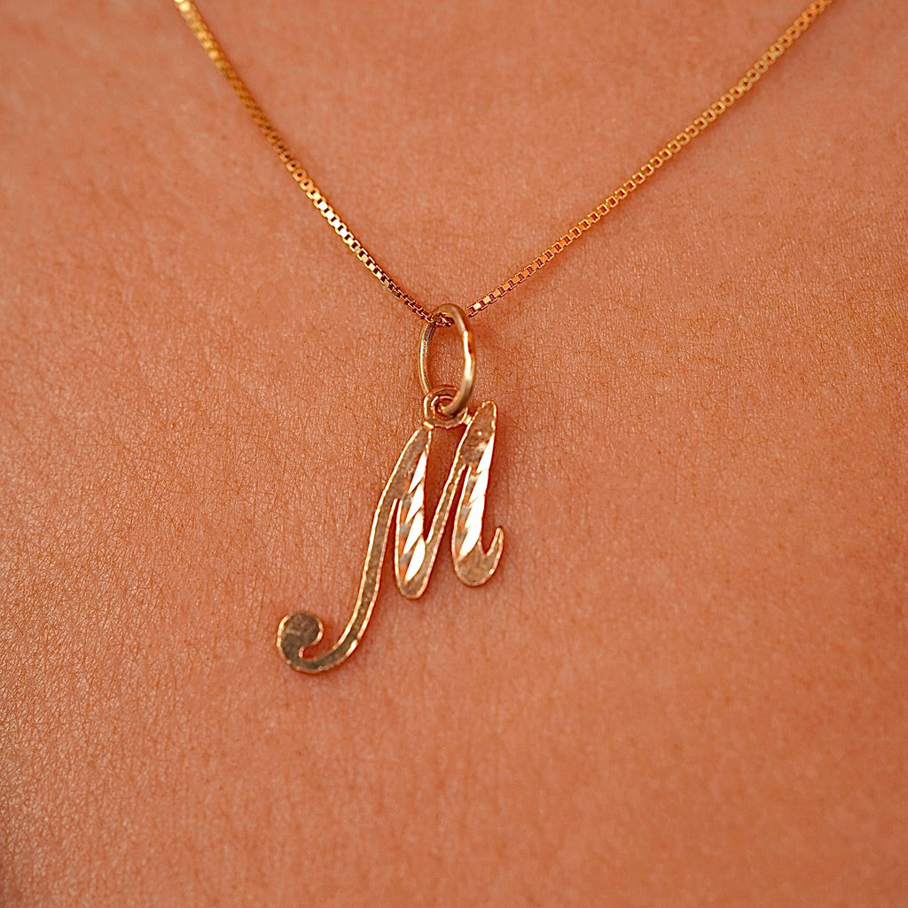 Model wearing a dainty gold initial M pendant, the charm sitting gracefully on her collarbone for a simple and personalized look.