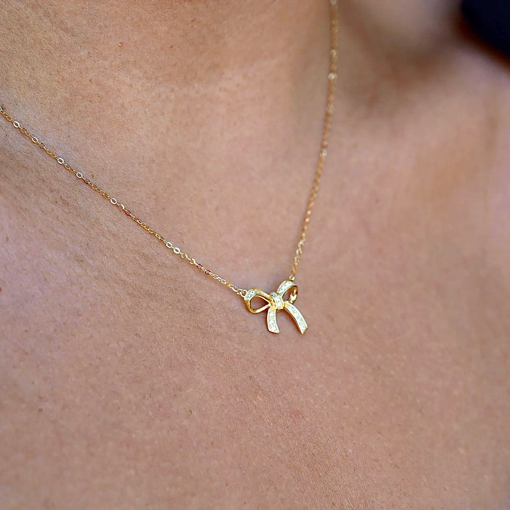 Model wearing the 14K gold ribbon necklace, capturing its dainty charm and graceful fit around the neckline.