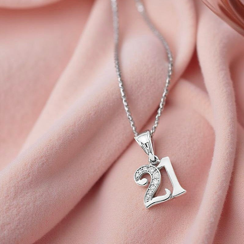 14K white gold '21' pendant with sparkling CZ accents displayed on soft pink velvet fabric, highlighting its elegant shine and detailed craftsmanship.