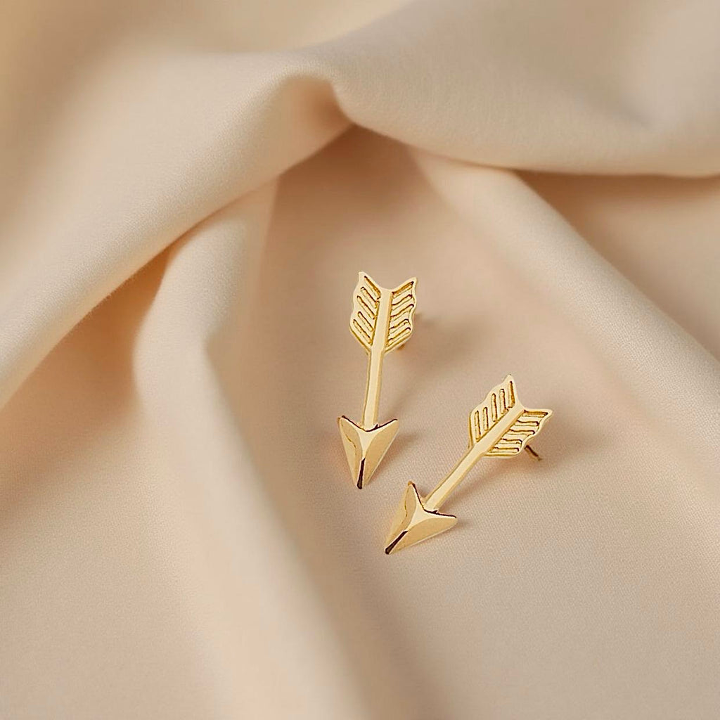 Pair of 14K gold arrow earrings displayed on neutral fabric, showcasing their minimal and sleek form with a refined polished shine.