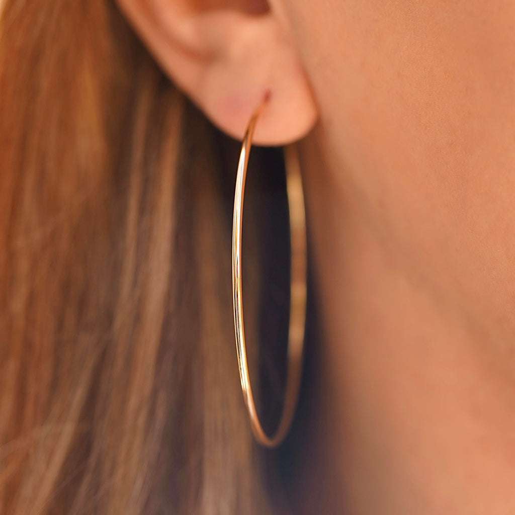 A model wearing 14K Yellow Gold 1.5mm Endless Hoop Earrings (55mm), highlighting their large size and elegant style for everyday wear.