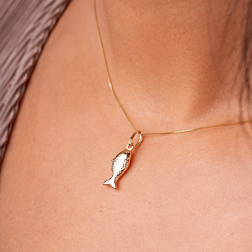 A woman wearing the 14K Gold Fish Charm Pendant on a delicate gold chain, highlighting its elegant shine and dainty size as it rests gracefully on her collarbone.