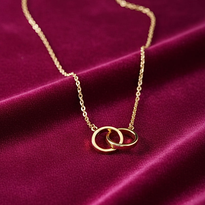 14K yellow gold ‘Together’ necklace laid on magenta velvet, with the rich fabric highlighting the smooth interlocking design and shine of the gold.