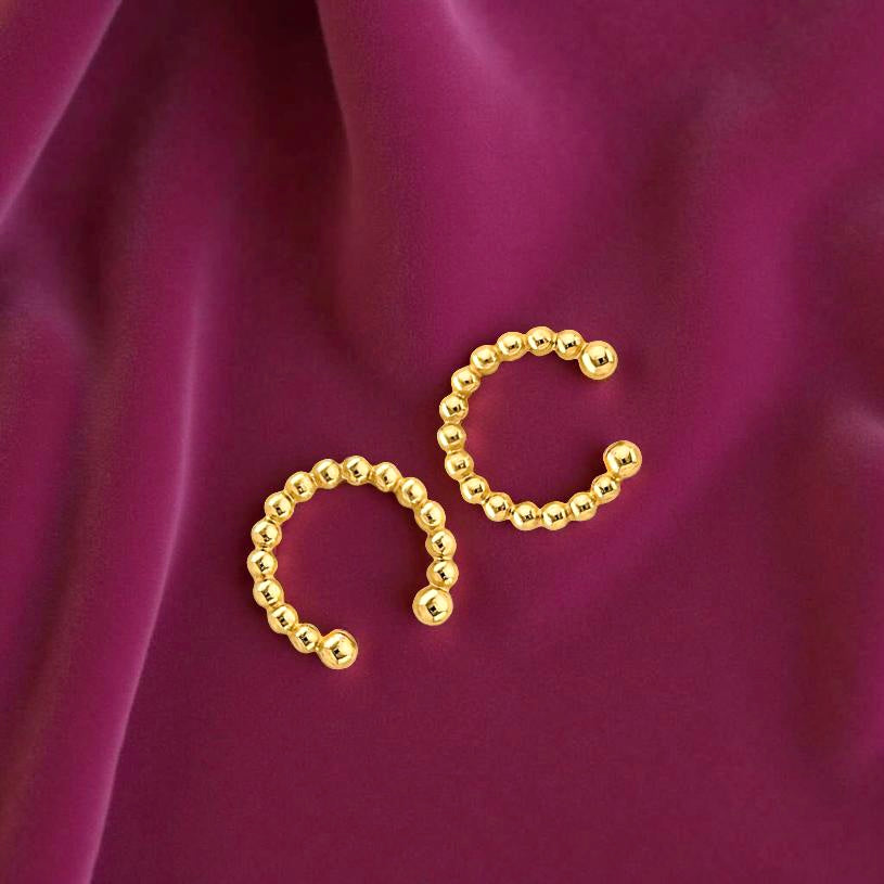 Minimalist 14K gold ear cuff displayed on a magenta velvet surface, featuring beaded detailing and bright luster.