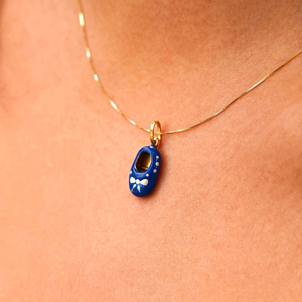A model wearing a delicate 14K gold baby shoe pendant with blue enamel on a thin gold chain. The pendant is the focal point, elegantly styled and perfect for daily wear or special occasions, with the model showcasing its charm and grace.