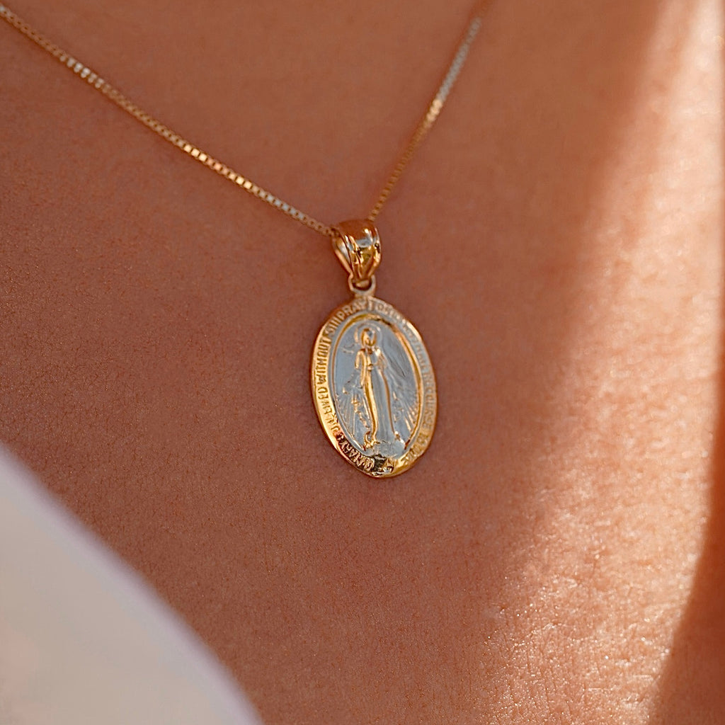 Model wearing a 14K gold Milagrosa pendant on a fine gold chain, the lightweight medallion resting at the collarbone, adding a subtle yet meaningful touch of faith.
