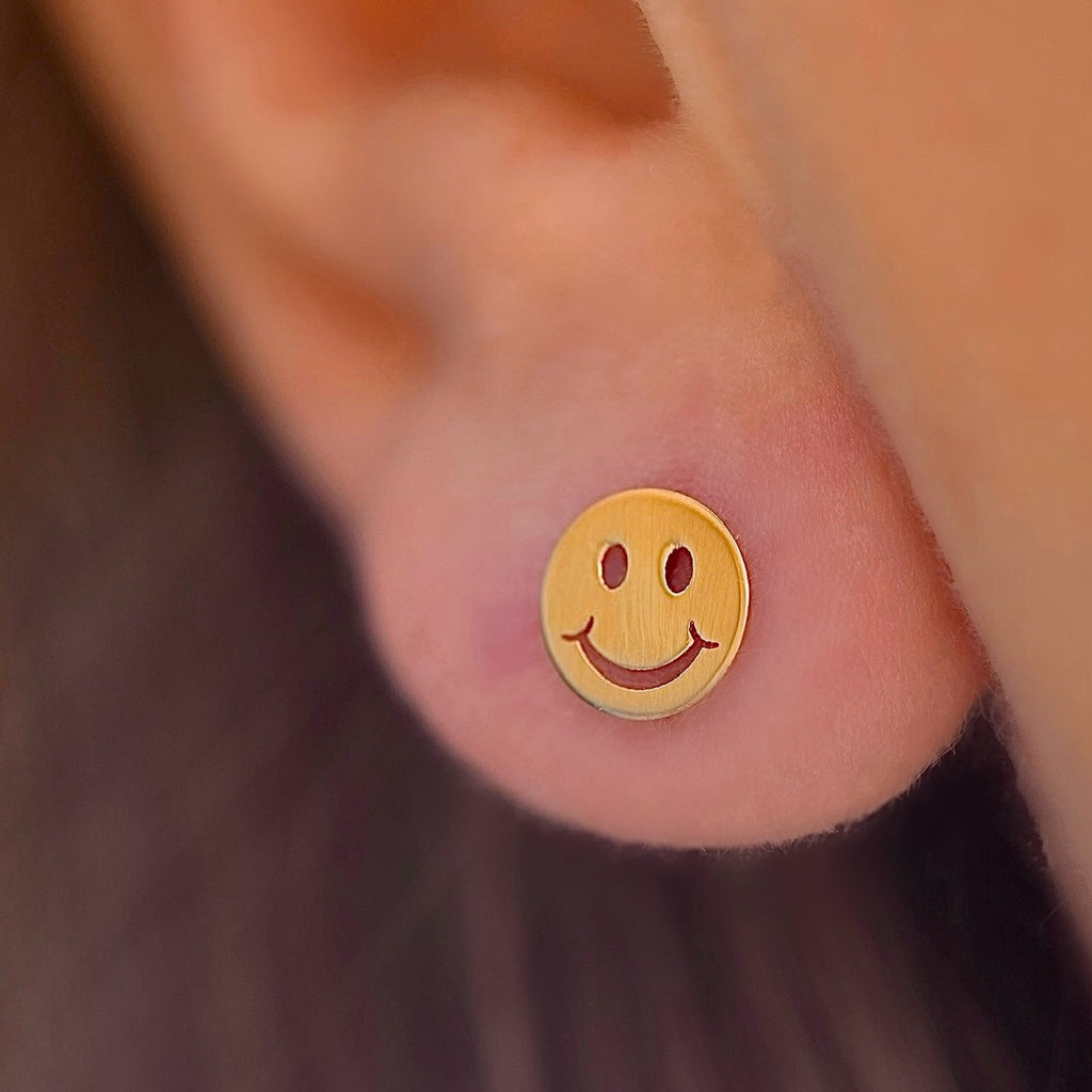 Close-up of a model wearing the 14K Yellow Gold Smiling Emoji Stud Earrings, showcasing their fun and playful design with a secure screw-back closure.