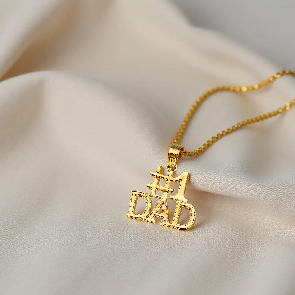 4K Yellow Gold #1 Dad Pendant resting on off-white fabric, showing polished gold and bold lettering.