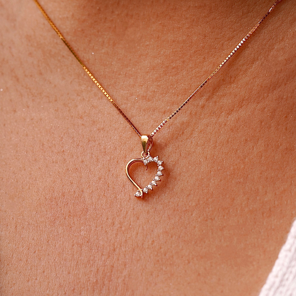 A delicate 14K Gold CZ Heart Pendant worn on a fine chain, elegantly resting against a model’s neckline, highlighting its dainty and elegant design.