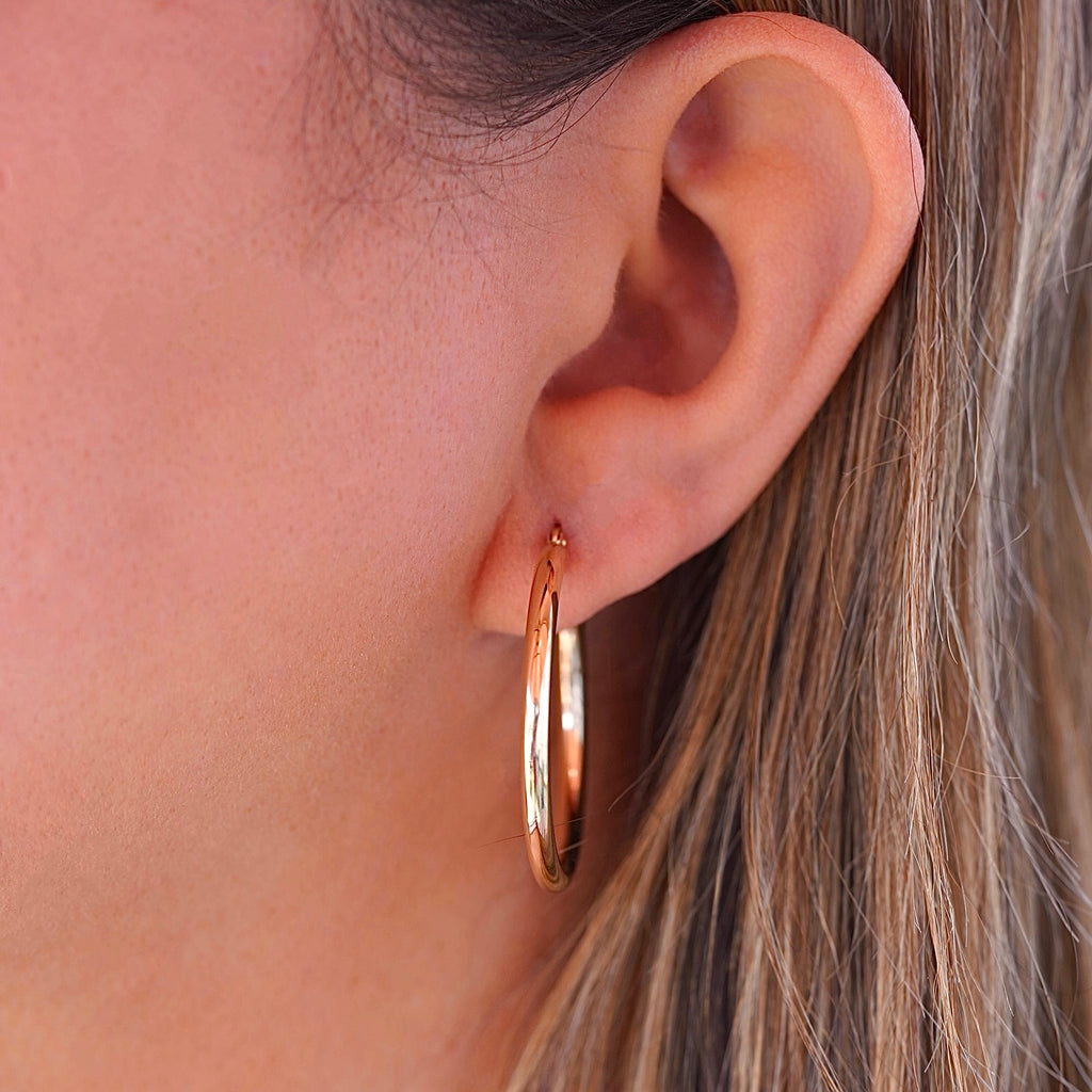 A stylish woman wearing 14K gold hoop earrings in yellow and white gold, adding a touch of sophistication to her everyday look.