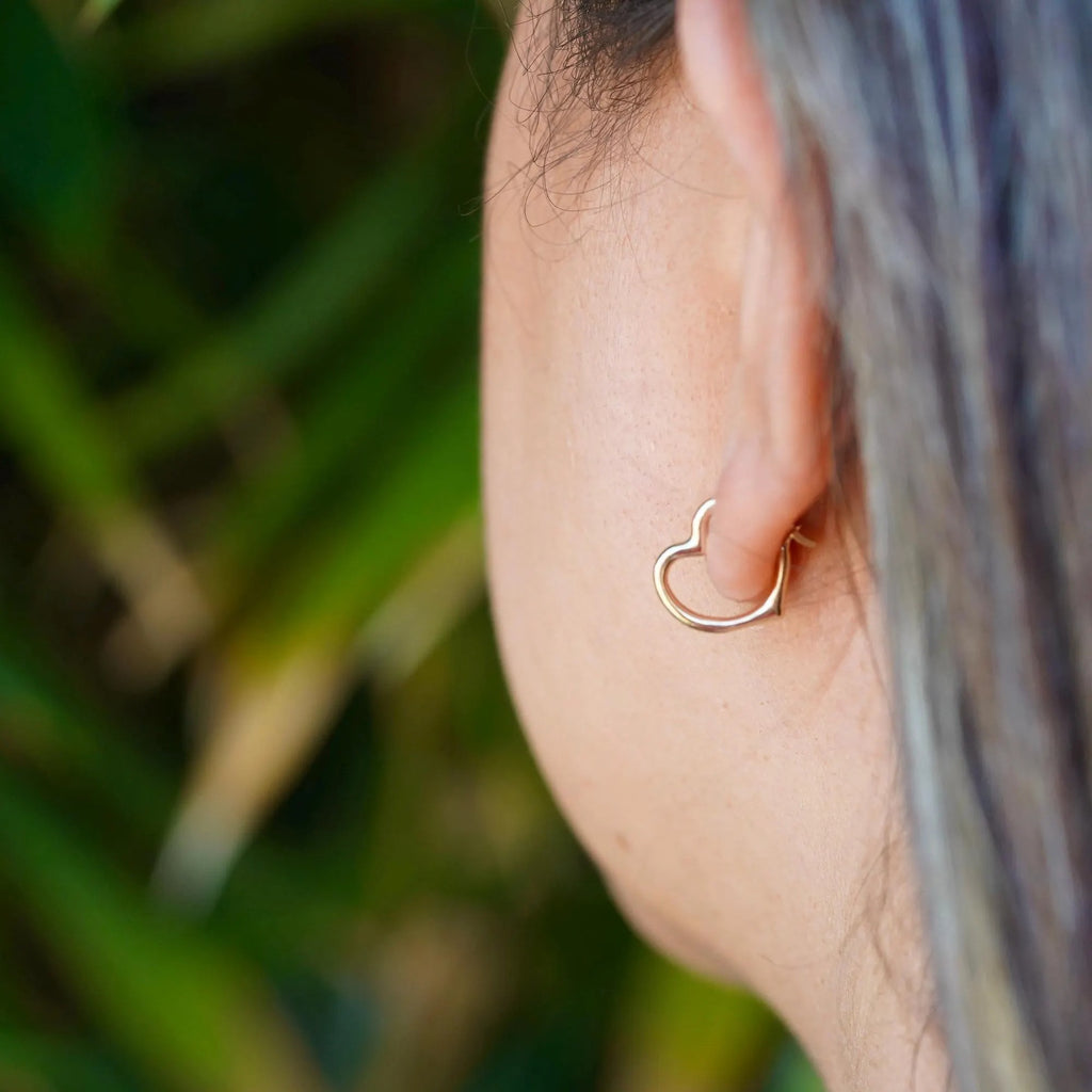 Model wearing dainty 14K yellow gold heart hoop earrings, with a radiant shine, highlighting the elegance and minimalist design of the earrings against a soft, natural background.