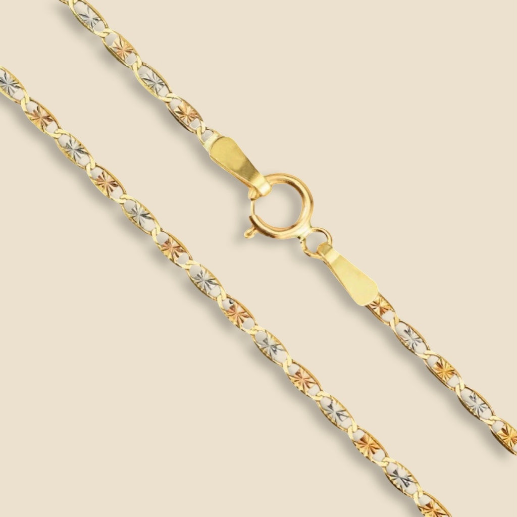 A close-up of a 14K tri-color Valentino chain laid on a plain background, showcasing its intricate links in rose, white, and yellow gold.