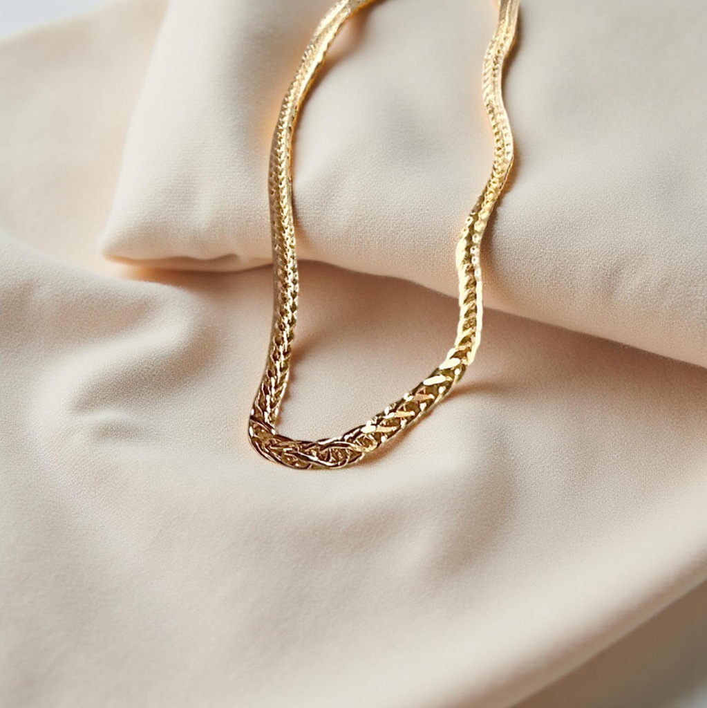 Delicate 14K yellow gold wheat chain with diamond-cut shine, laid gracefully on a textured off-white fabric background for a soft, elegant presentation.