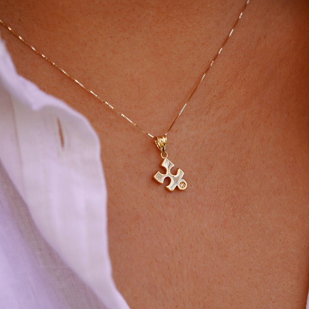 A model gracefully wears the 14K gold puzzle piece pendant on a fine chain, showcasing its subtle elegance and timeless design. The charm rests beautifully against the skin, adding a touch of meaning and sophistication to any outfit.