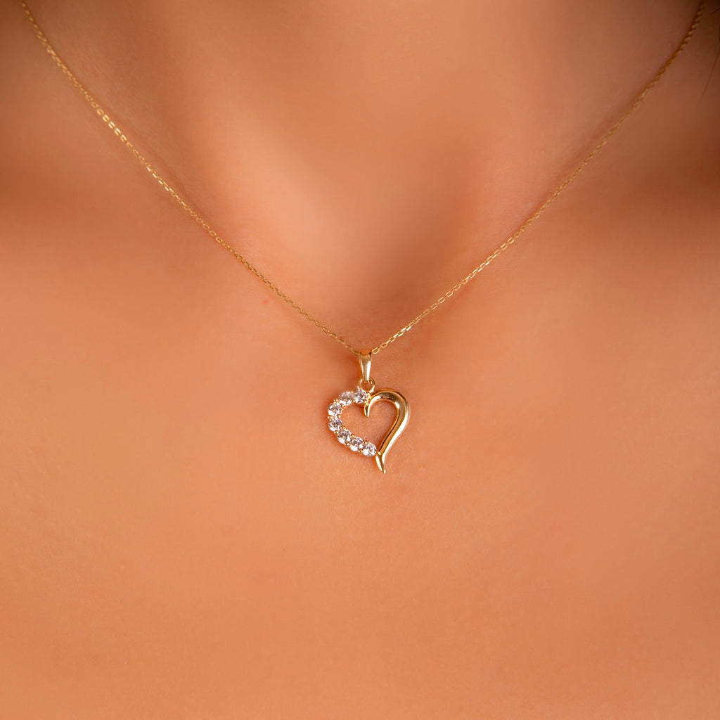 A delicate 14K Solid Yellow Gold Tiny Heart Pendant worn by a model, elegantly resting on a fine gold chain. The charm’s minimalist heart shape and sparkling cubic zirconia catch the light, adding a touch of love and sophistication to any outfit.