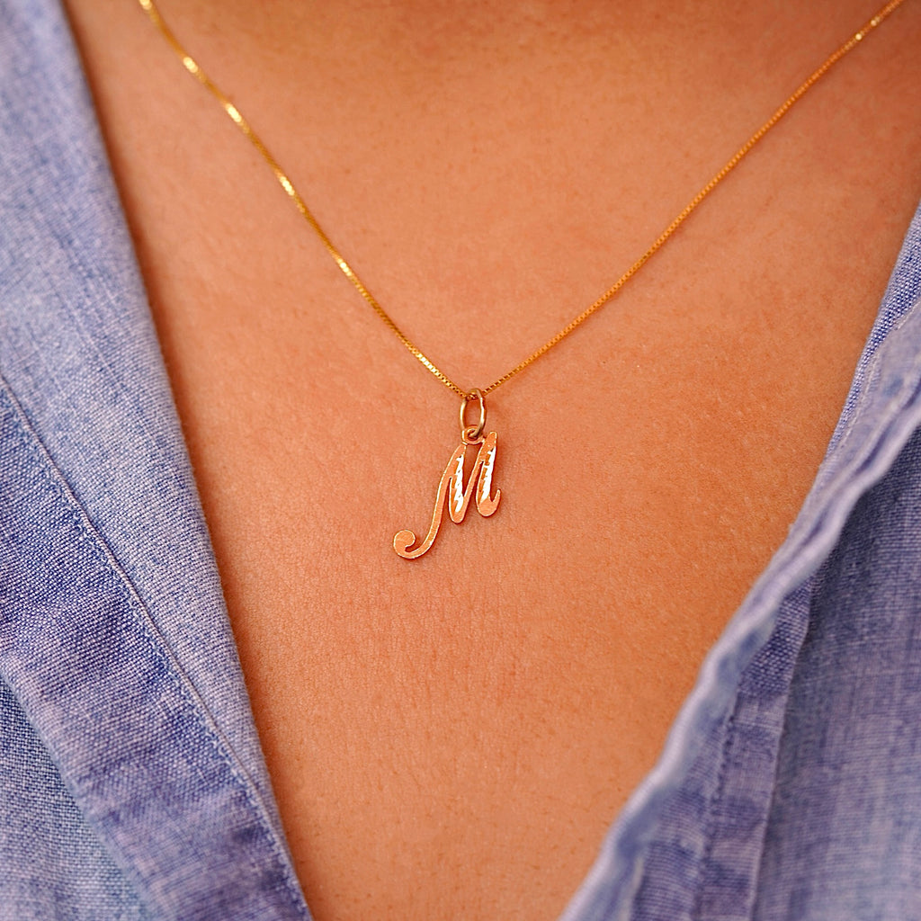 Model wearing a dainty gold initial M pendant, the charm sitting gracefully on her collarbone for a simple and personalized look.