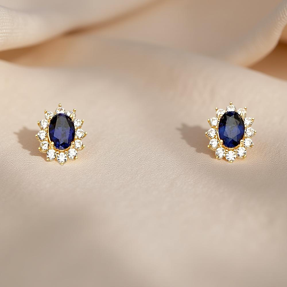 A pair of 14K yellow gold blue stone earrings displayed on soft, off-white linen fabric, highlighting the elegant gold tones and rich blue center stones.