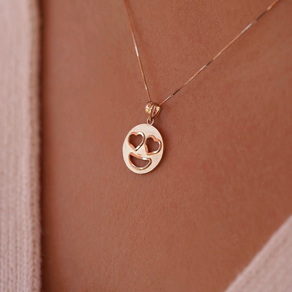 Model wearing 14K gold heart eyes emoji pendant on a delicate gold chain, showing how the charm sits beautifully at the neckline for everyday elegance.