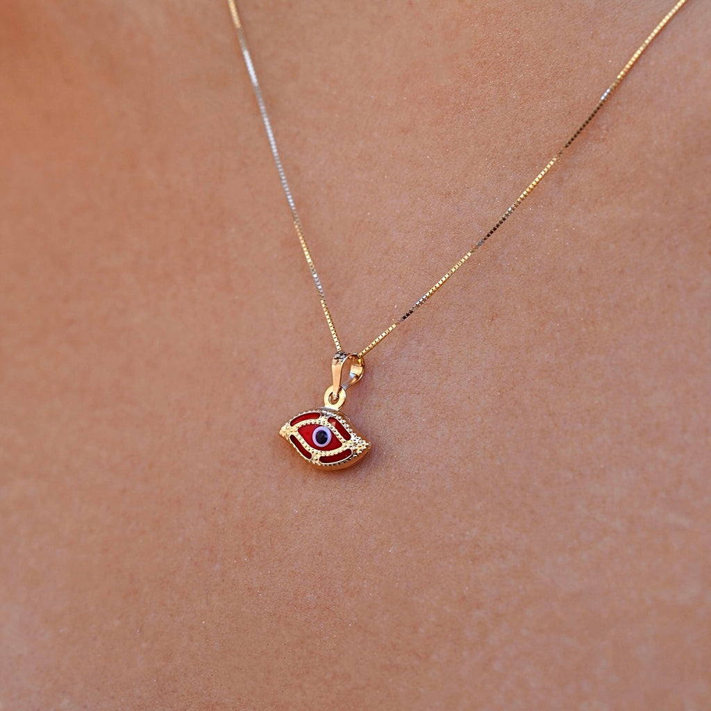 A model wearing a delicate 14K yellow gold red evil eye pendant featuring a brilliant red cubic zirconia center, resting elegantly on her neckline. The fine gold chain and polished finish reflect soft light, highlighting the pendant’s symbolic protection and timeless charm.