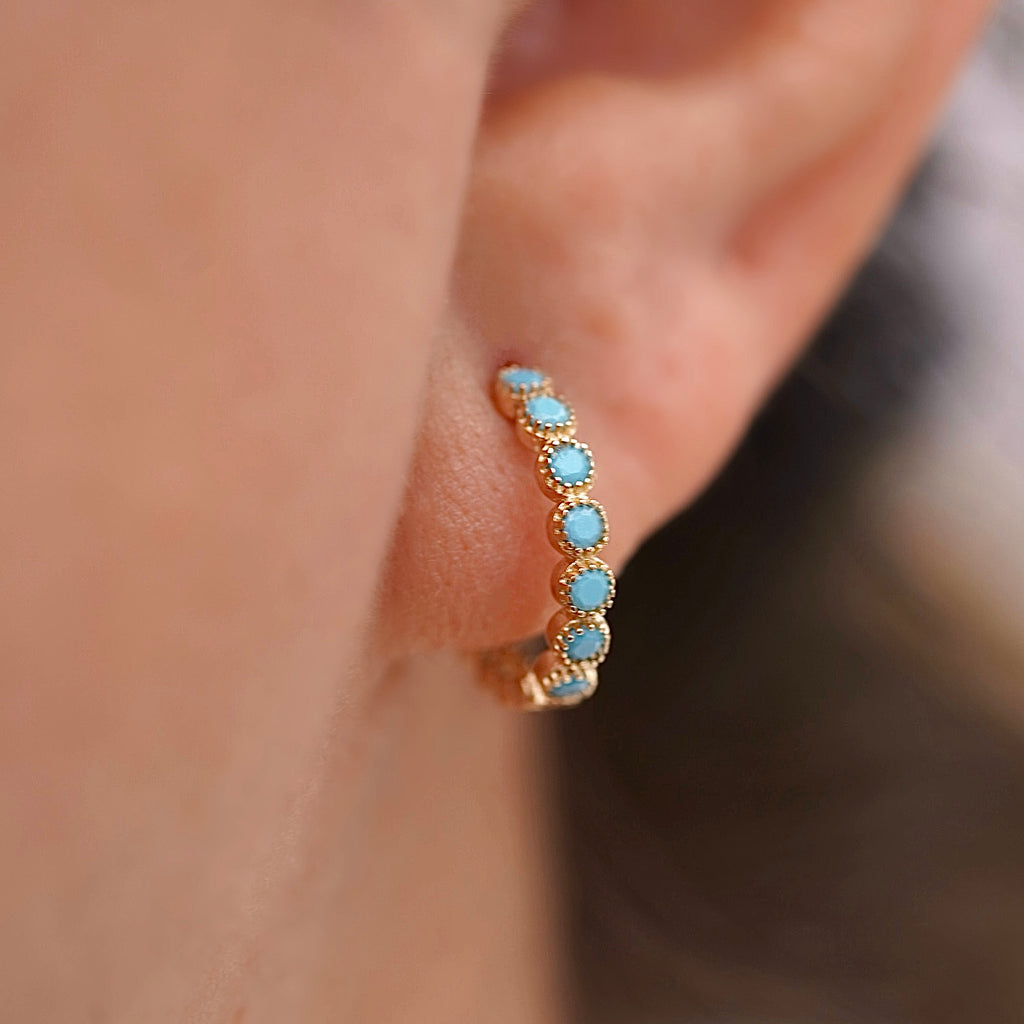 Side profile of a model wearing 14K yellow gold round turquoise Huggies earrings, highlighting the delicate hoops with turquoise accents hugging her earlobe, styled with casual outfit for an elegant everyday look.