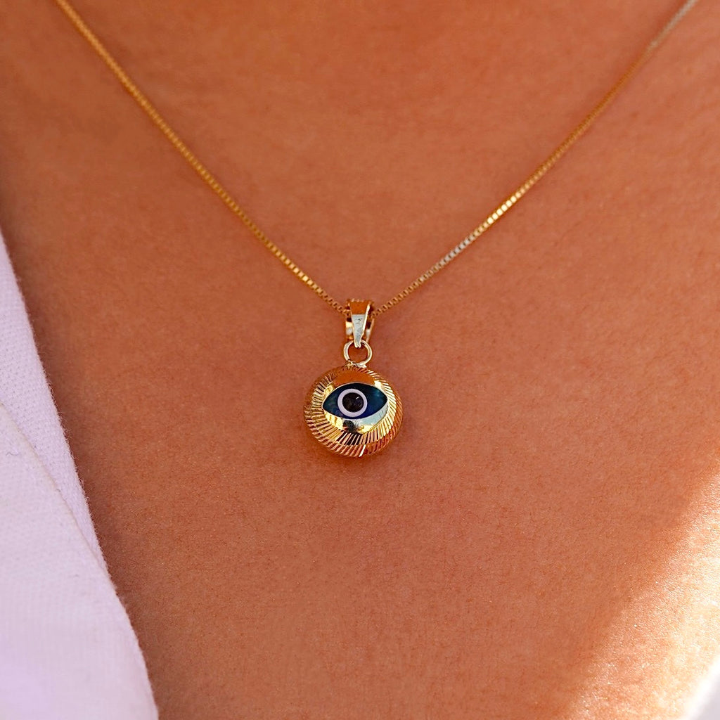 A model wears the 14K gold evil eye pendant with blue center on a fine chain, showcasing its dainty size and symbolic beauty as it rests just below the collarbone.