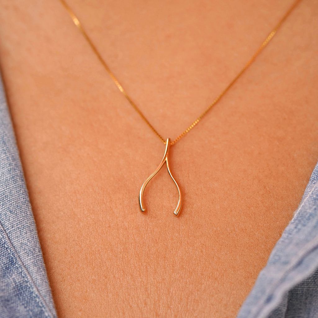 Model wearing the 14K gold wishbone pendant on a delicate chain, demonstrating its dainty size and elegant everyday look.